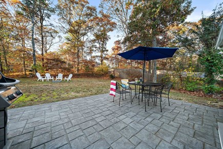 Mashpee Cape Cod vacation rental - Back yard - stamped patio, dining table/umbrella, Weber gas grill