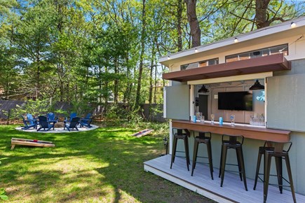 Centerville Cape Cod vacation rental - Backyard in the day - Bar shed, firepit, games and greenery